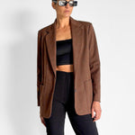 Person wearing a brown blazer over a black top and pants on a white background