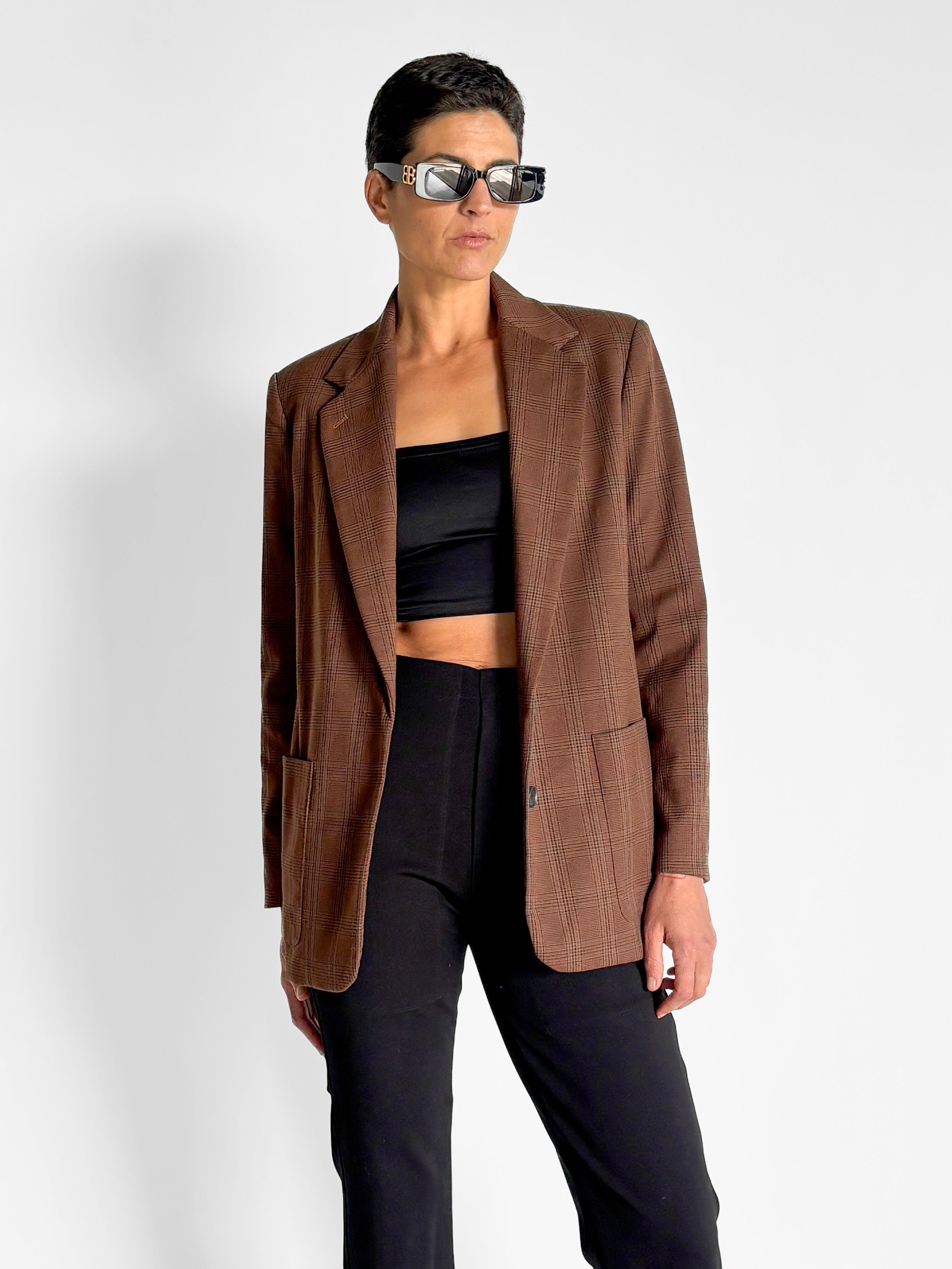 Person wearing a brown blazer over a black top and pants on a white background